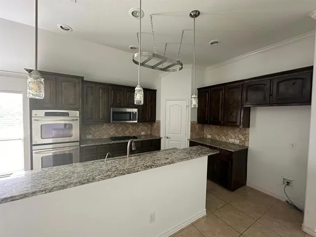 a kitchen with kitchen island granite countertop stainless steel appliances a sink a refrigerator a stove a microwave and cabinets