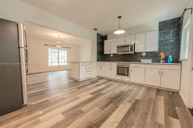 a kitchen with stainless steel appliances granite countertop a refrigerator a sink dishwasher a stove and white cabinets with wooden floor