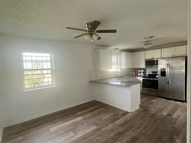 a kitchen with granite countertop a refrigerator a sink dishwasher a stove and white cabinets with wooden floor