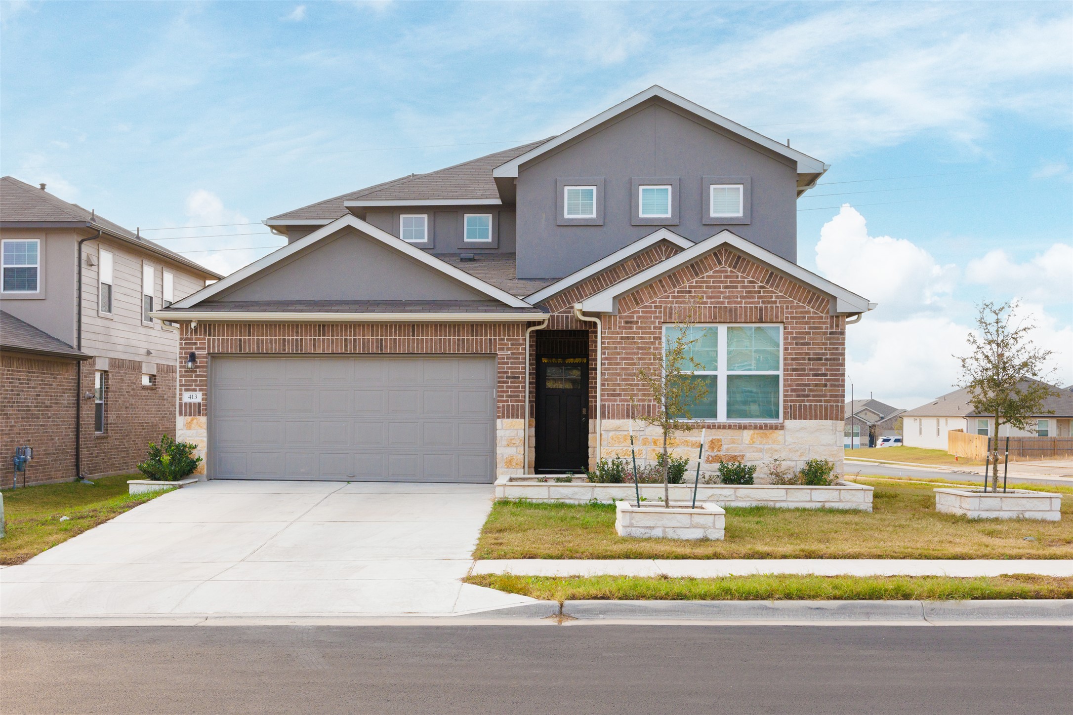 View of front of house featuring stone siding, driveway, brick siding, a front yard, and stucco siding
