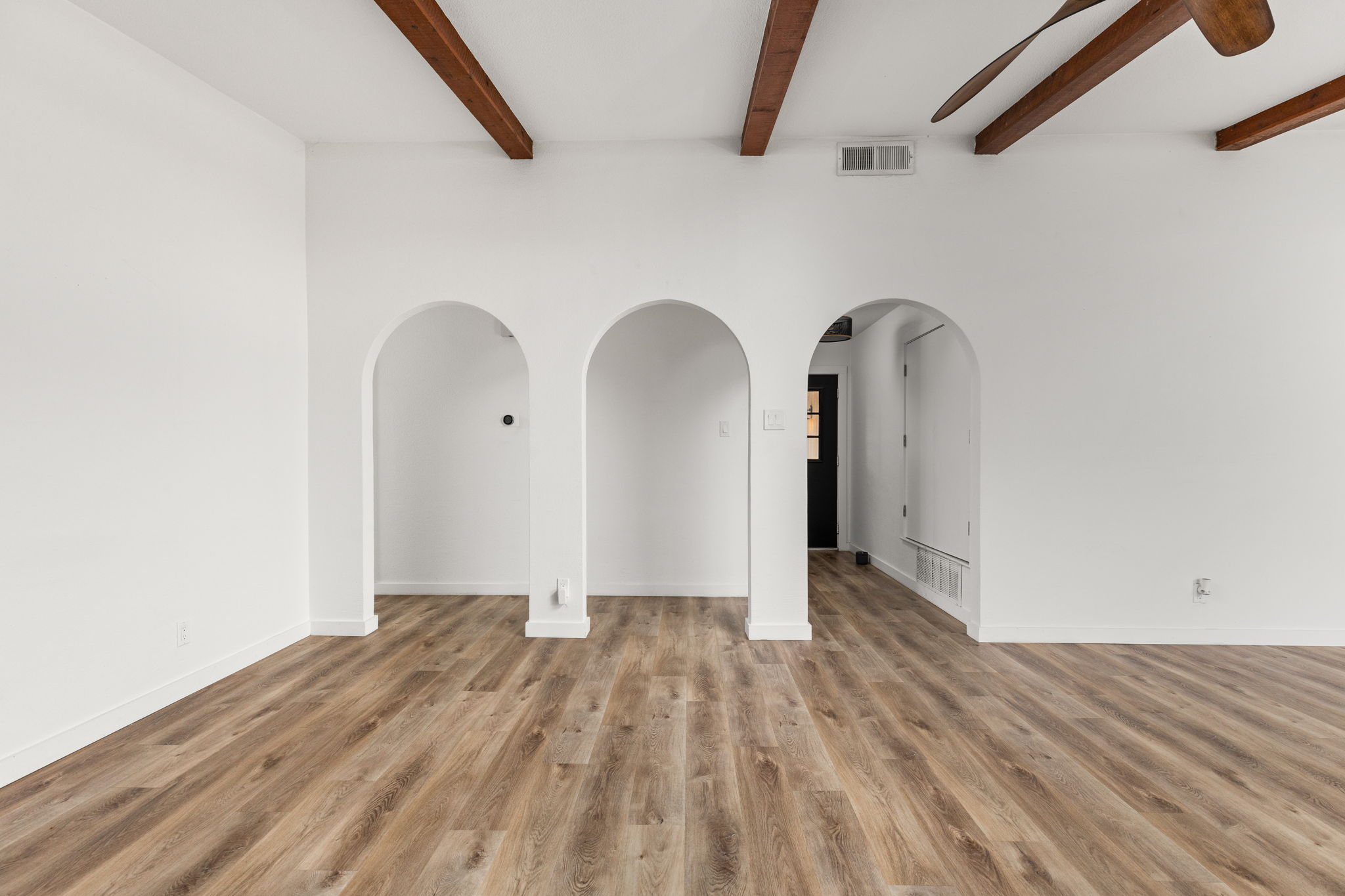 612 Meadowbrook Drive Georgetown, TX 78628 - Photo 10 of 35 Empty room with arched walkways, light wood-style flooring, and beamed ceiling