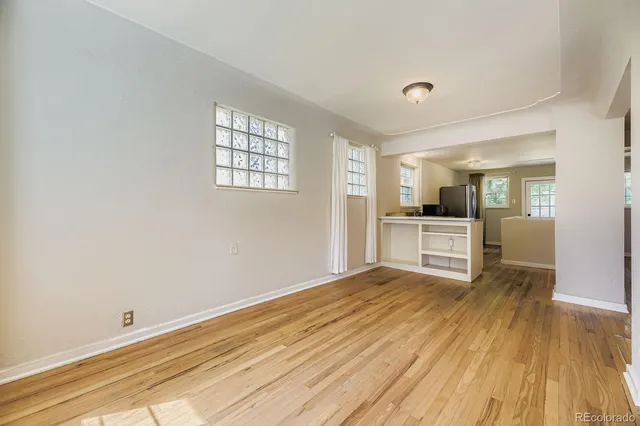 a view of empty room with wooden floor and kitchen