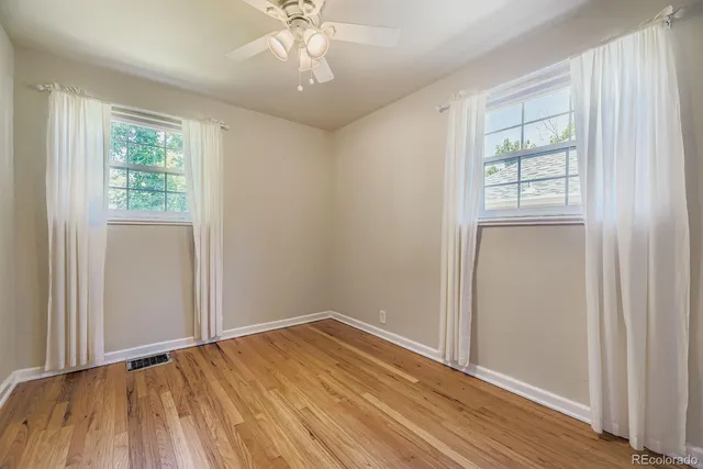 a view of empty room with wooden floor and fan