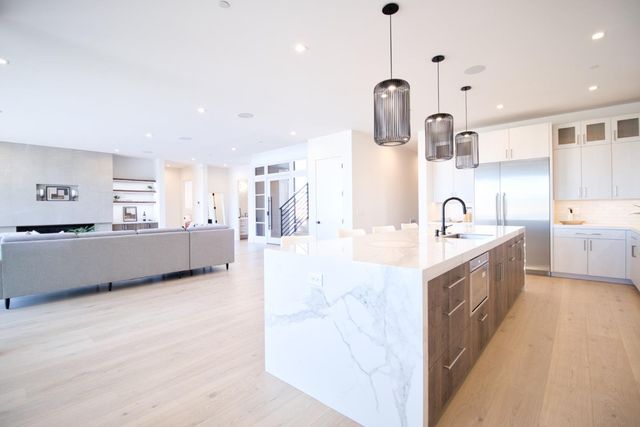 a large white kitchen with a large counter top a sink a window and stainless steel appliances