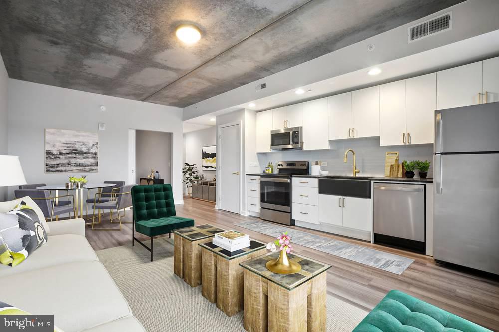 1901-39 Callowhill Street, Unit 912 Philadelphia, PA 19130 - Photo 12 of 17 a kitchen with stainless steel appliances kitchen island granite countertop a stove a refrigerator a sink dishwasher a dining table and chairs with wooden floor