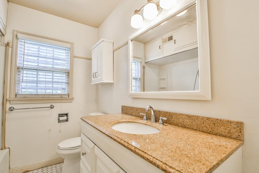 2318 29th Street Lubbock, TX 79411 - Photo 26 of 32 a bathroom with a granite countertop sink toilet and mirror
