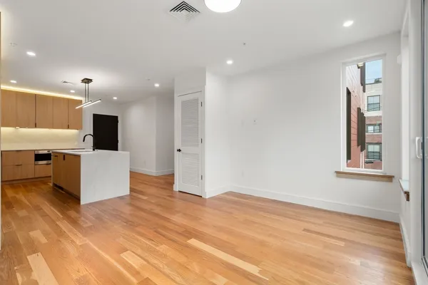 an empty room with kitchen view and wooden floor