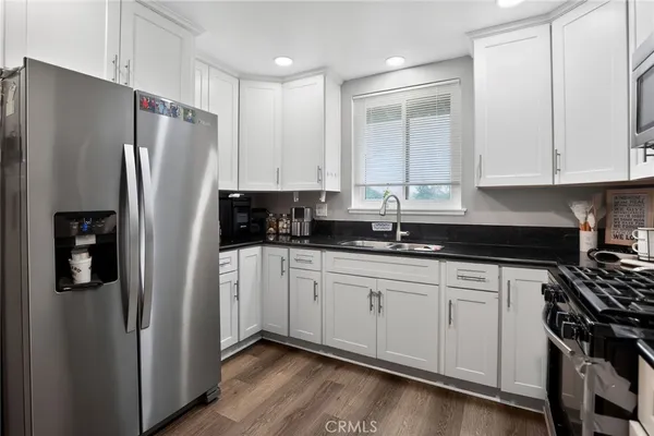 a kitchen with stainless steel appliances granite countertop a refrigerator a sink and white cabinets
