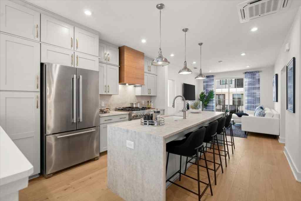 a kitchen with stainless steel appliances kitchen island granite countertop a refrigerator a sink dishwasher a dining table and chairs with wooden floor