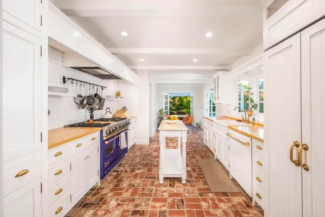 a large white kitchen with granite countertop a sink a stove a chimney wooden floor and a dining table