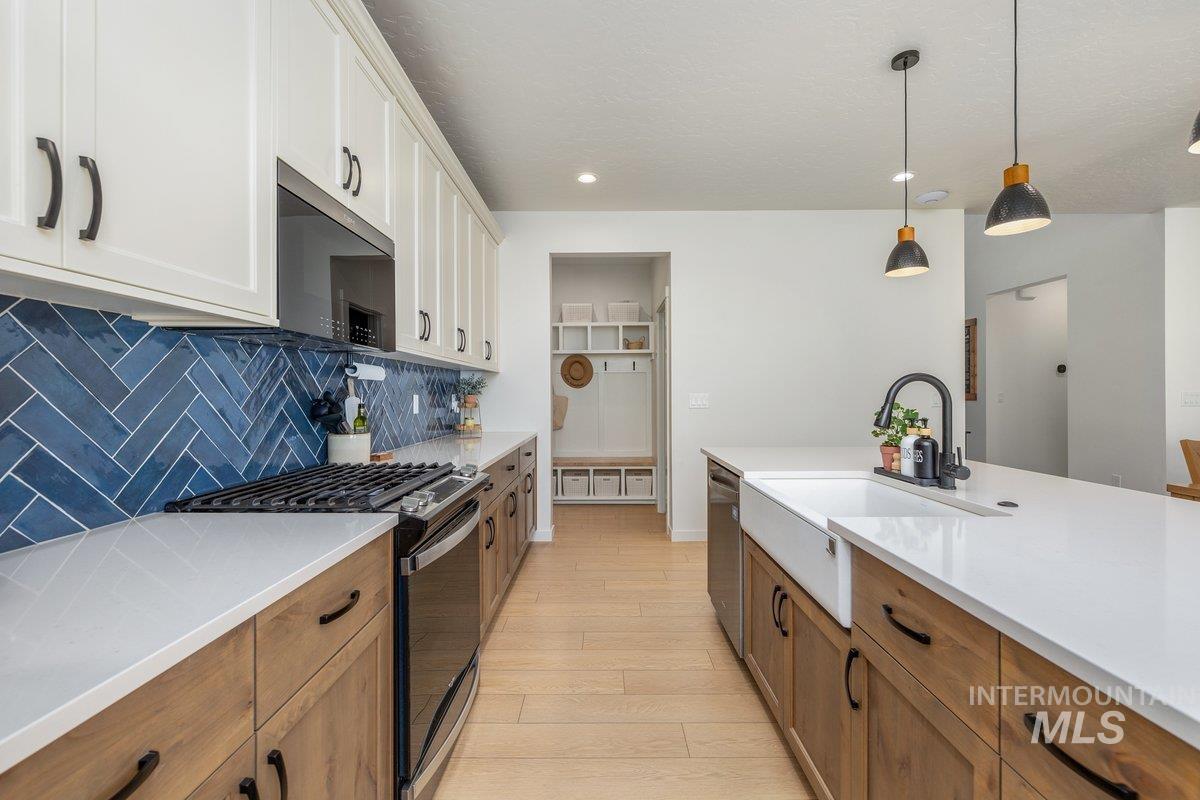 1380 West Chilitna Street Meridian, ID 83642 - Photo 9 of 50 Modern kitchen featuring a white farmhouse sink, contrasting wood-finish and white cabinetry, a striking blue herringbone tile backsplash, and light wood-finish flooring