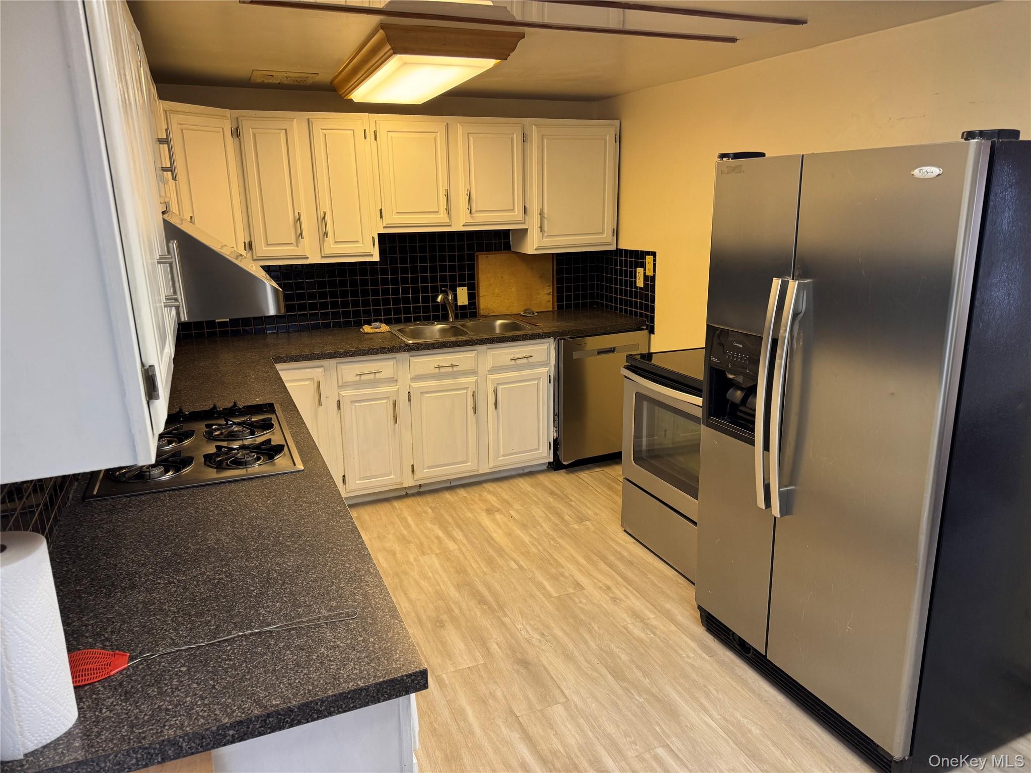 96 White Roe Lake Road Livingston Manor, NY 12758 - Photo 17 of 31 The kitchen features white cabinetry, dark countertops, a black tiled backsplash, and stainless steel appliances