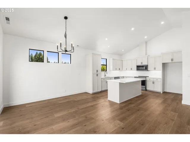 a large white kitchen with kitchen island a sink wooden floor and a refrigerator