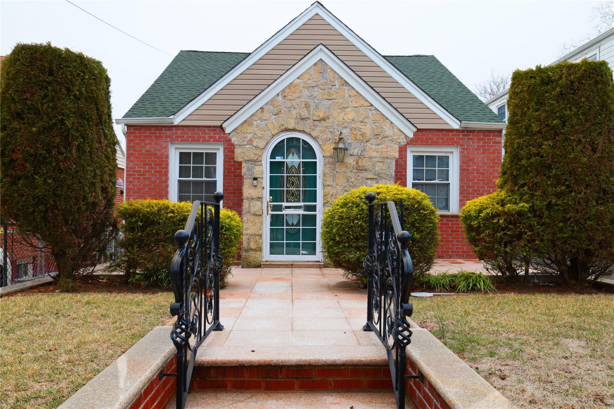 221-10 114th Road Queens, NY 11411 - Photo 1 of 1 View of front facade with stone siding, a shingled roof, and a front yard