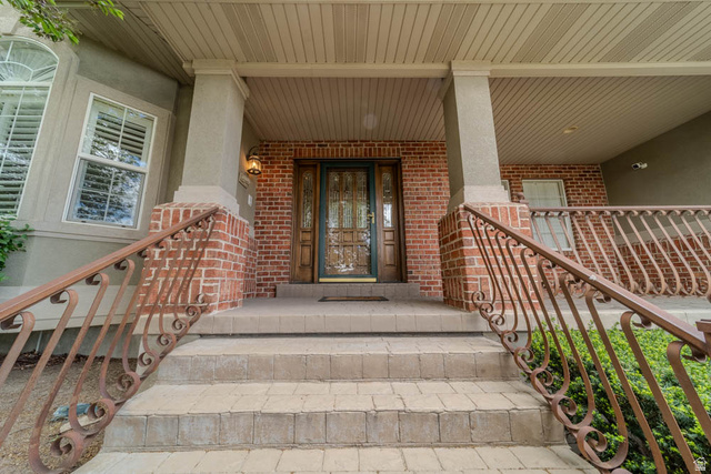 598 Hollow Creek Road Draper, UT 84020 - Photo 15 of 110 Covered brick entry with an ornate wood-paneled door featuring decorative glass inserts, complemented by detailed iron railings and textured paver steps