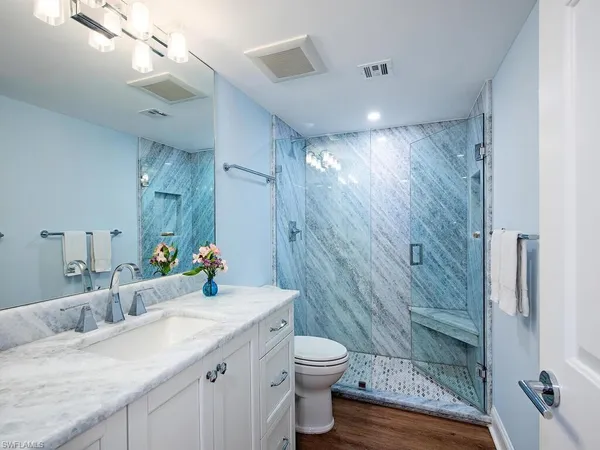 a bathroom with a granite countertop sink a toilet a mirror and shower