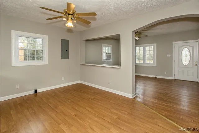 an empty room with wooden floor chandelier fan and windows