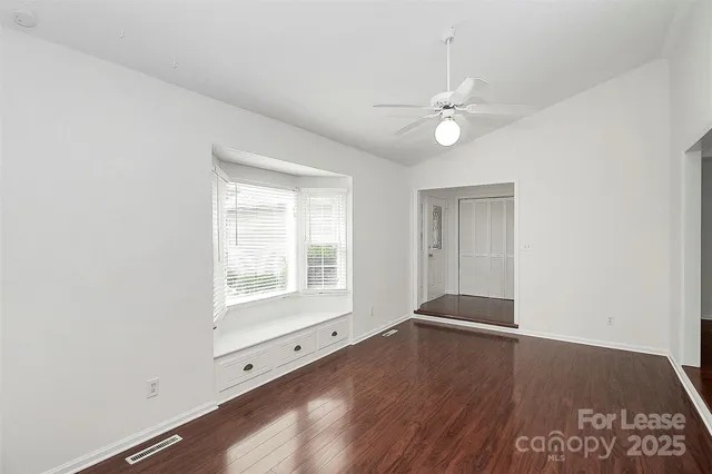 an empty room with wooden floor ceiling fan and windows