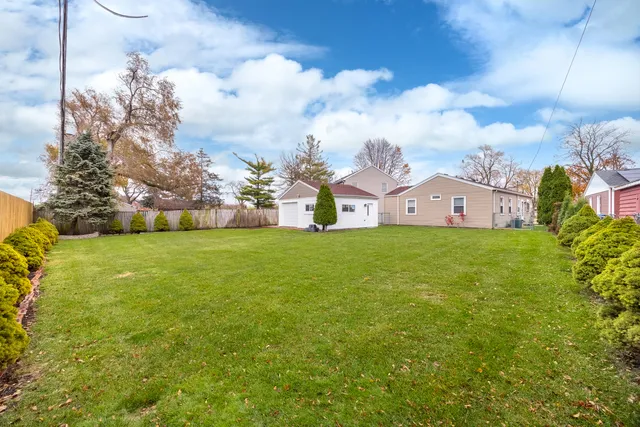 a view of a house in front of a big yard with plants and large tree