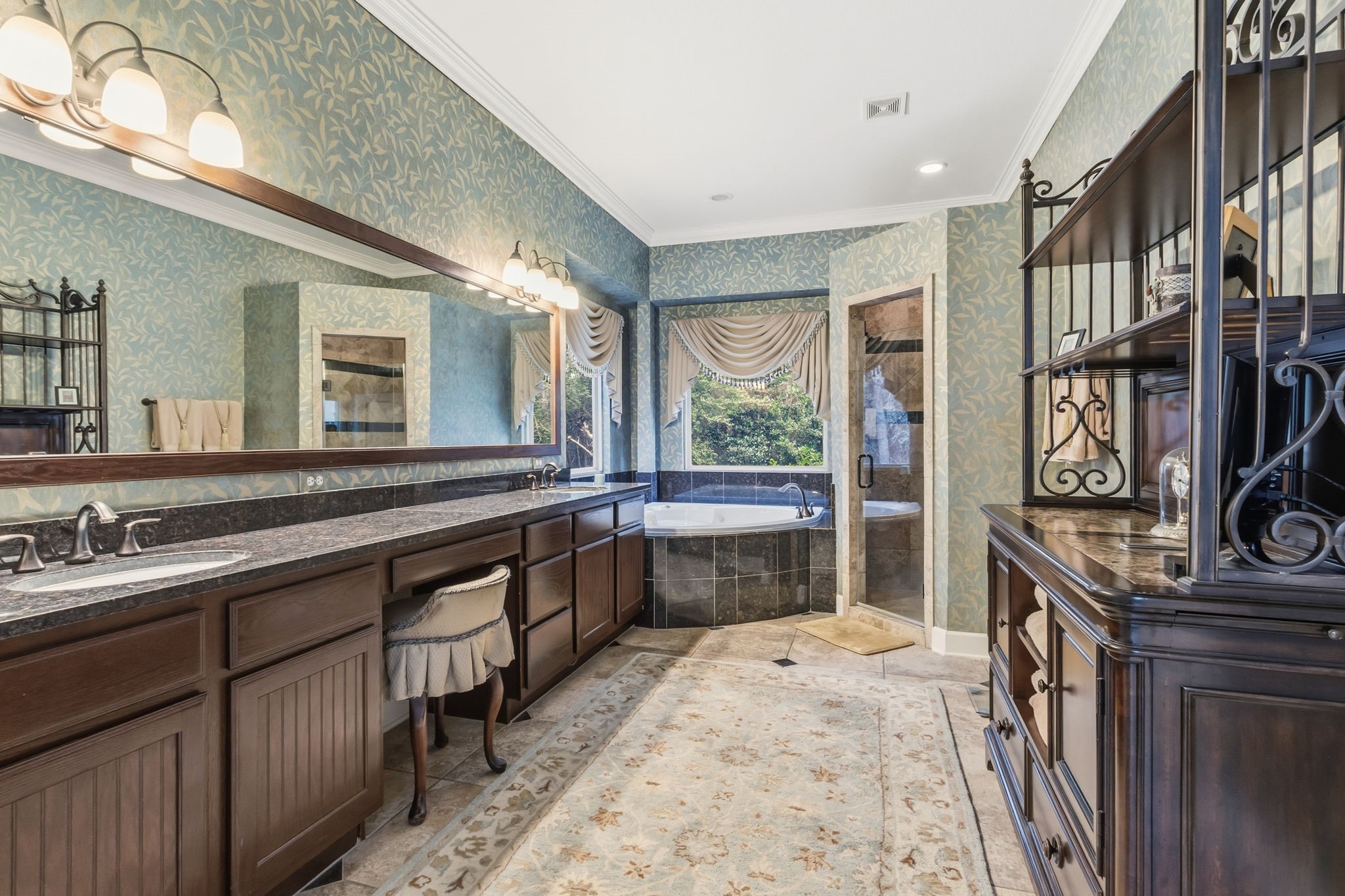 7514 Saddle Blanket Drive Waller, TX 77484 - Photo 25 of 50 This spacious bathroom features elegant dark wood cabinetry, a long granite countertop with dual sinks, and warm lighting. It includes a luxurious corner bathtub with a picturesque window view and a separate glass-enclosed walk in shower.