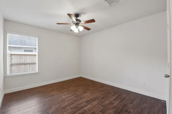 an empty room with wooden floor fan and windows
