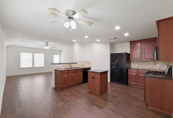 a kitchen with stainless steel appliances granite countertop a refrigerator a sink dishwasher a stove and a dining table with wooden floor