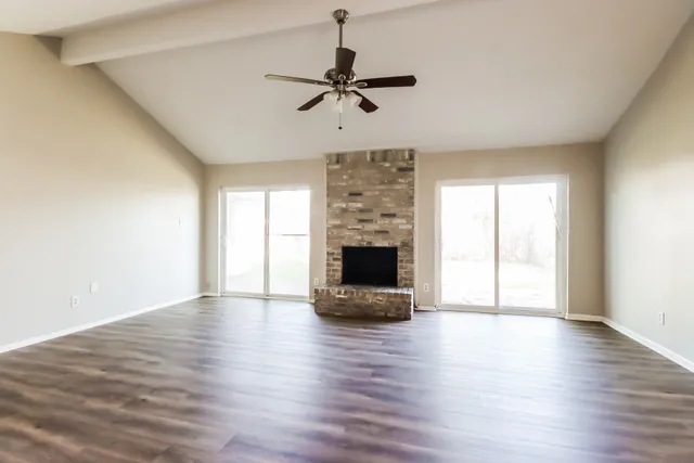 a view of a livingroom with a fireplace a ceiling fan and windows