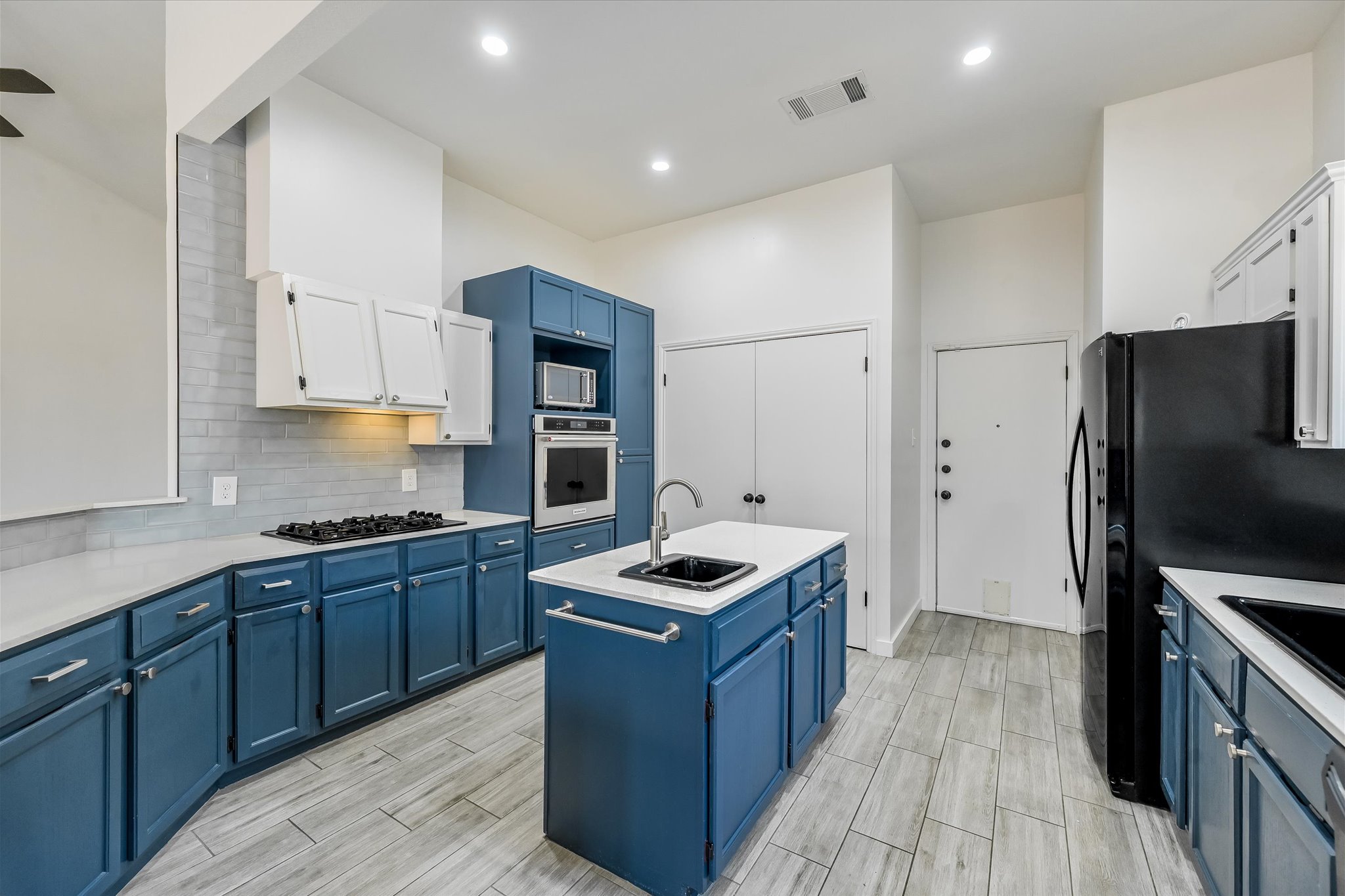 10203 Brantley Bend Austin, TX 78748 - Photo 8 of 20 Kitchen with a center island with sink, wood tiled floors, stainless steel appliances, dual tone cabinets, and decorative backsplash