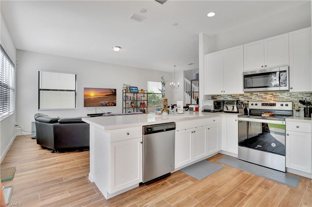 9041 Madrid Circle Naples, FL 34104 - Photo 28 of 32 a kitchen with stainless steel appliances white cabinets a sink a stove a microwave and wooden floors
