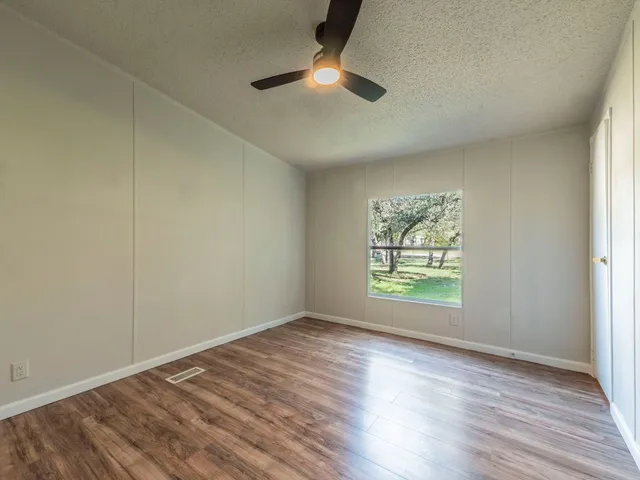 an empty room with wooden floor chandelier fan and windows