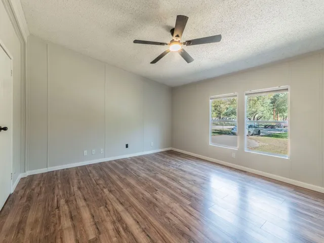 an empty room with wooden floor fan and windows