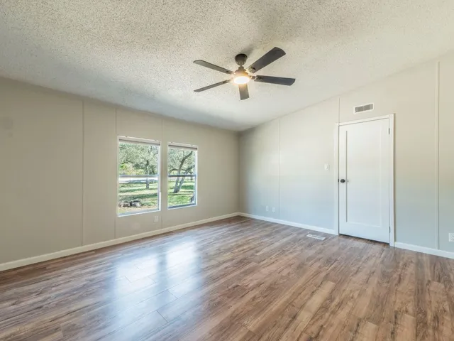 an empty room with wooden floor fan and windows