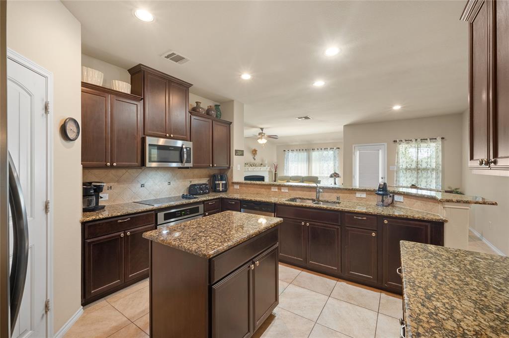 520 Rustic Oak Lane McKinney, TX 75072 - Photo 11 of 30 Open-concept kitchen featuring dark wood cabinetry, granite countertops, a central island, stainless steel appliances, and tile flooring
