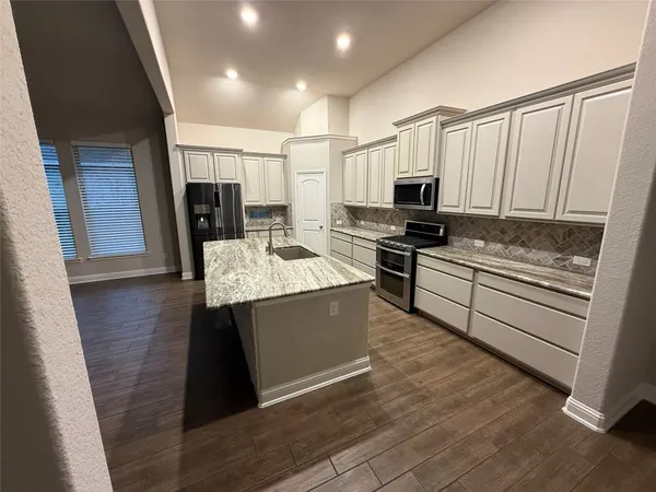 a kitchen with kitchen island granite countertop a stove top oven a sink a counter space and cabinets