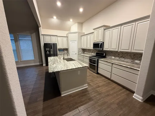 a kitchen with kitchen island granite countertop a stove top oven a sink a counter space and cabinets