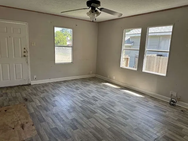 an empty room with wooden floor chandelier and windows