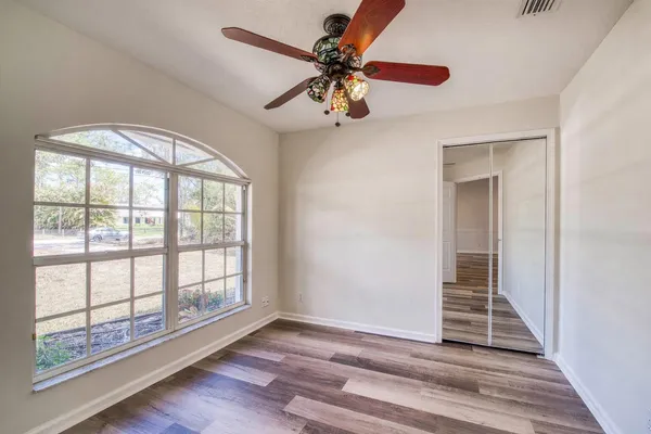 an empty room with wooden floor fan and windows