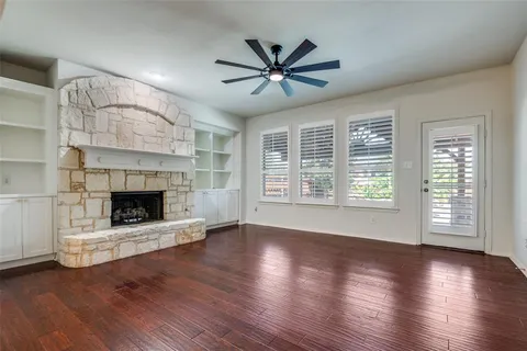 an empty room with wooden floor a fireplace a ceiling fan and windows
