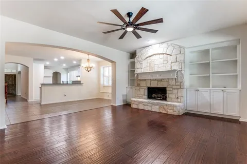an empty room with wooden floor a kitchen view and a fireplace