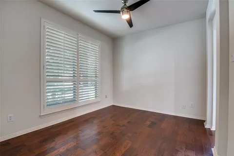 an empty room with wooden floor a ceiling fan and windows