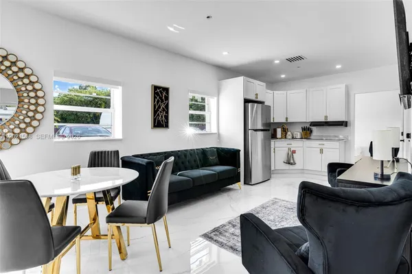 a kitchen with stainless steel appliances kitchen island granite countertop a dining table chairs and a refrigerator