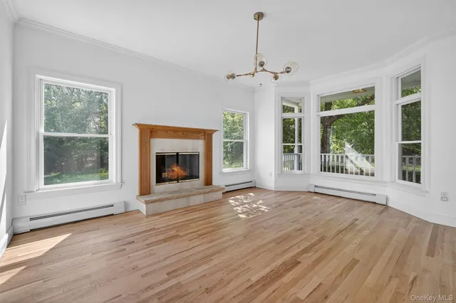 a view of an empty room with wooden floor fireplace and a window