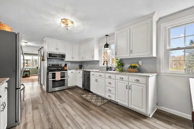 a kitchen with granite countertop a refrigerator a stove a sink and white cabinets with wooden floor