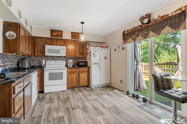 a kitchen with granite countertop a refrigerator a stove a sink and white cabinets with wooden floor