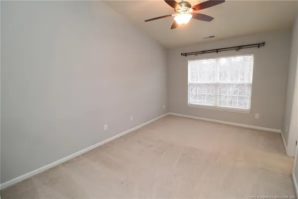 an empty room with chandelier fan and windows