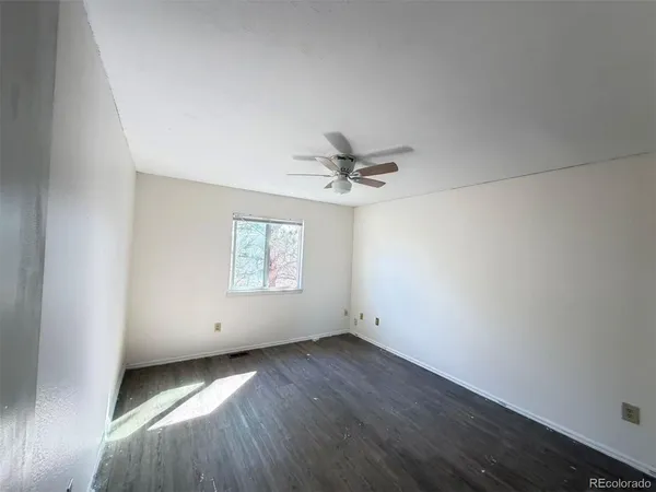 an empty room with wooden floor ceiling fan and windows
