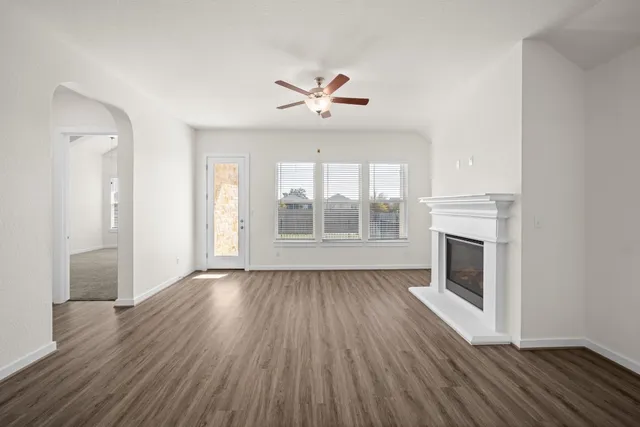 an empty room with wooden floor a ceiling fan a fireplace and windows