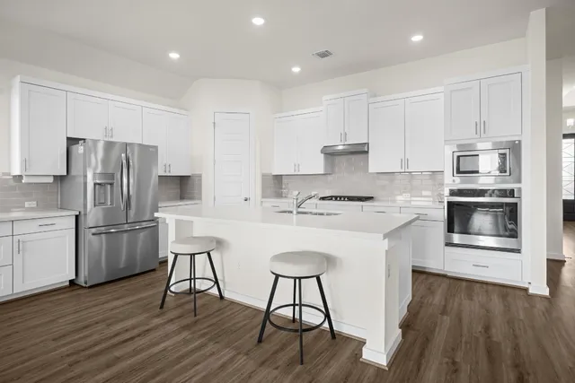 a kitchen with a refrigerator a stove top oven and white cabinets