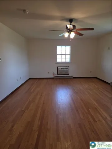an empty room with wooden floor chandelier fan and windows