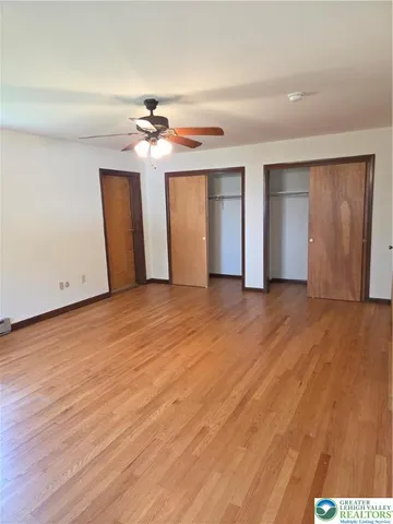 an empty room with wooden floor ceiling fan and windows